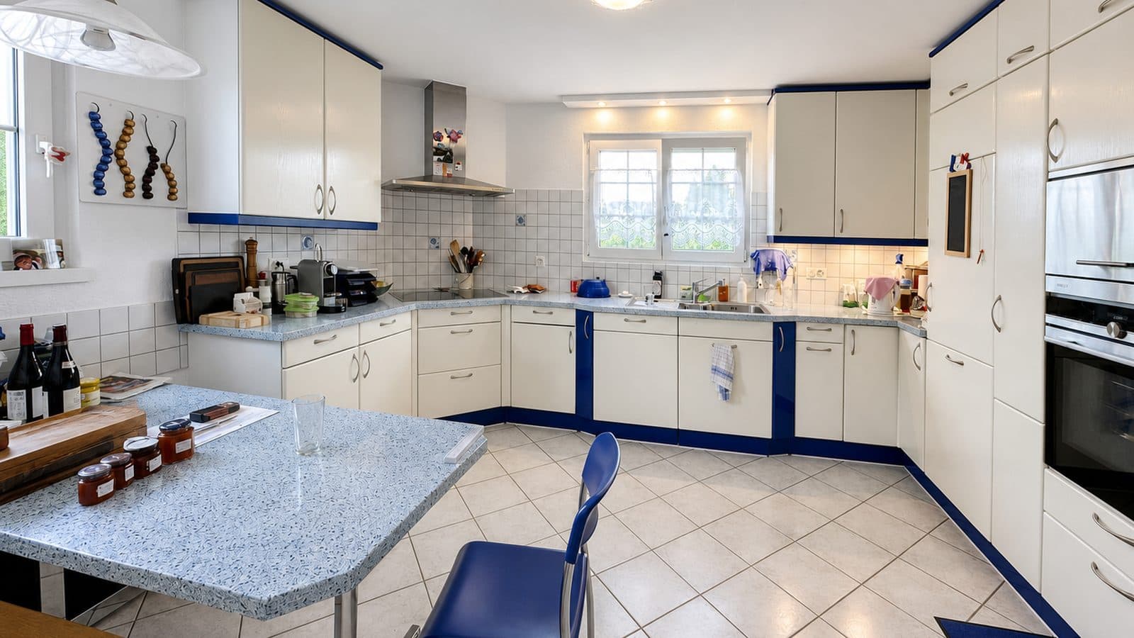 The kitchen before renovation: cream fronts with blue trims, speckled worktop, white wall tiles.
