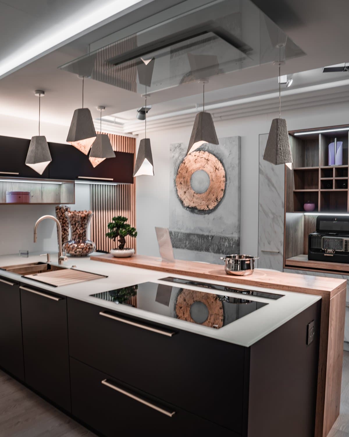 Black island with a cooktop, concrete pendants and wooden storage